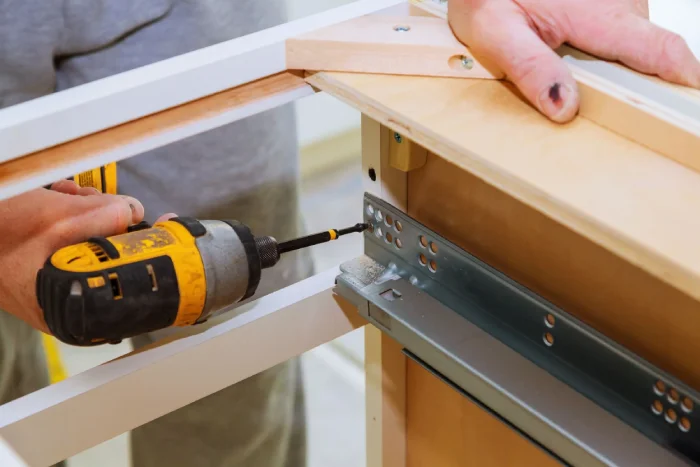 Close-up of a worker using a drill to install drawer runners.