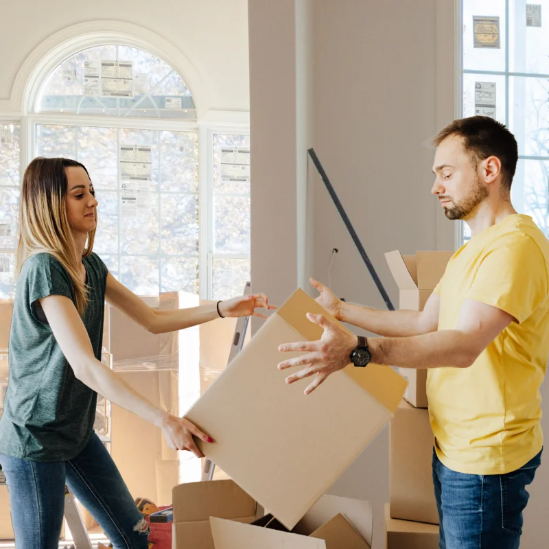 Young couple passing cardboard moving boxes to each other while unpacking.