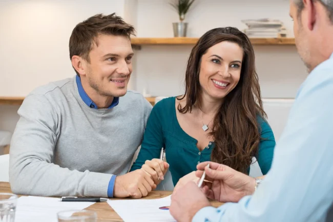 Homeowners smiling while reviewing kitchen remodel floor plan papers during a design consultation.