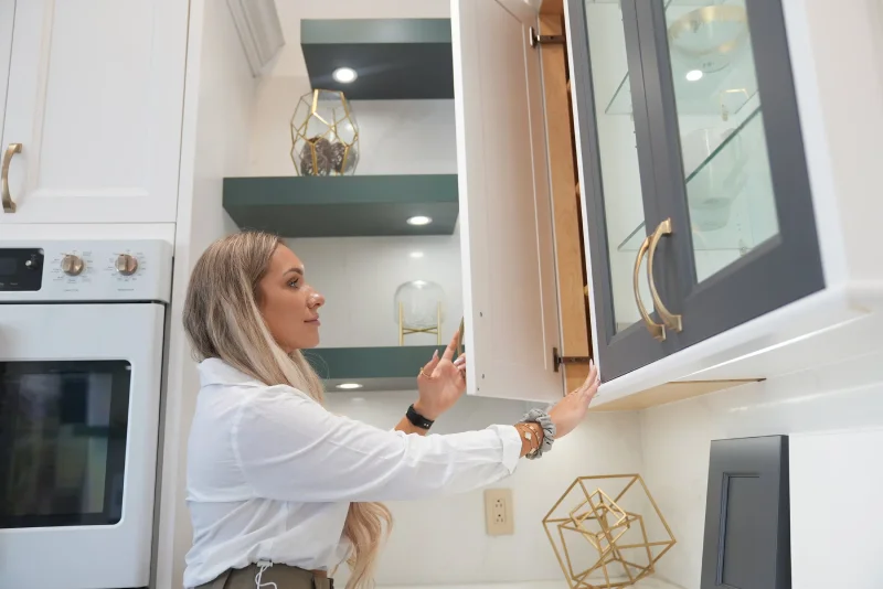 Female designer opening a glass front cabinet door in a kitchen showroom.
