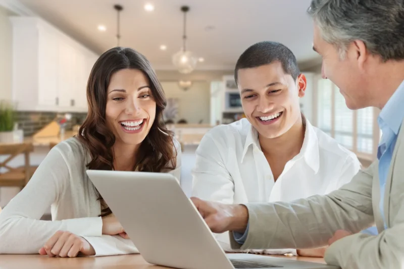 Smiling couple reviewing 3D kitchen design layouts on a laptop with a professional.