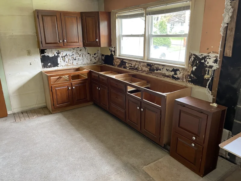 Professional tradesman assembling wood kitchen cabinets with tools in a factory.