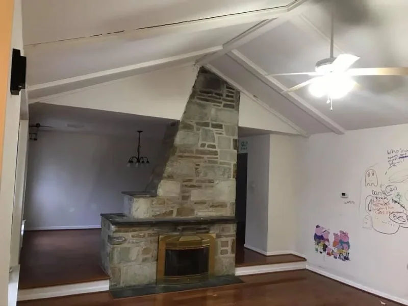 Empty residential living room featuring a large central stone fireplace.