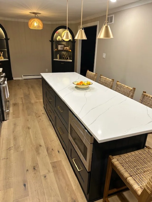 Long kitchen island with dark wood base panels and crisp white stone top.