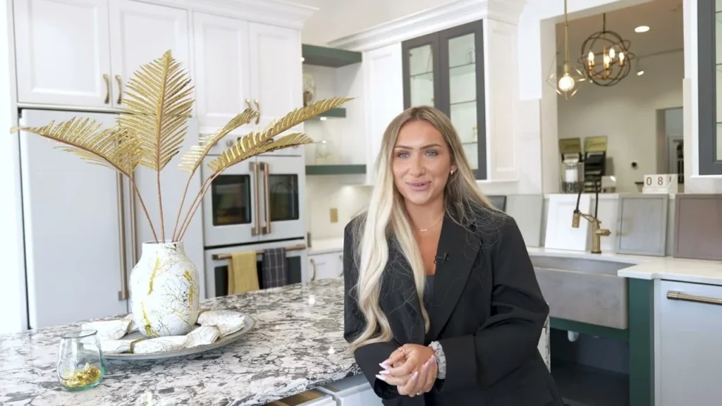 Female kitchen designer leaning against a granite island countertop.