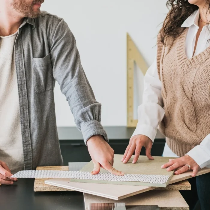 Cropped shot of design professionals adjusting wood material samples over a dark countertop surface.