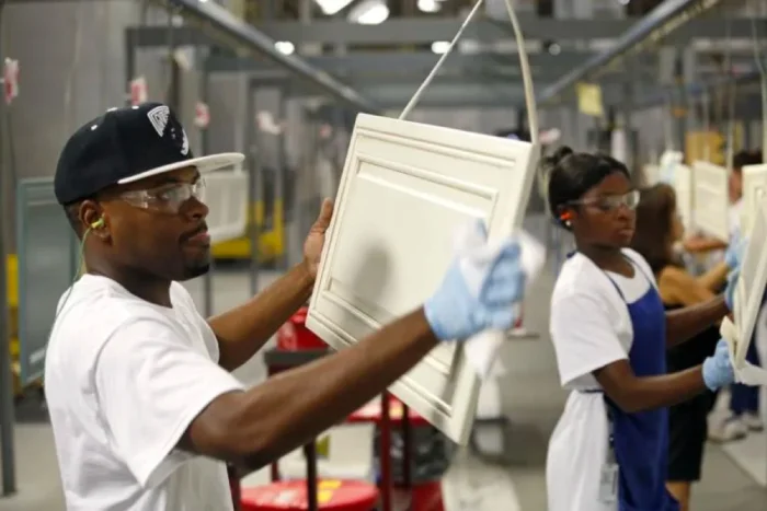 Factory worker holding a white shaker cabinet door on production line.