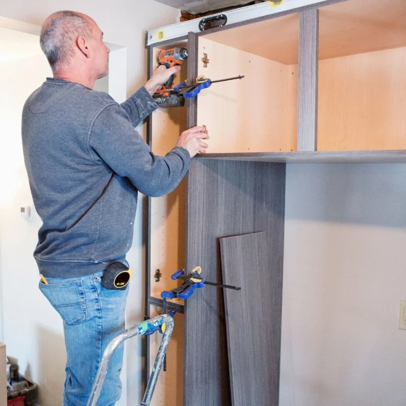 Carpenter using a drill to install custom kitchen cabinets.