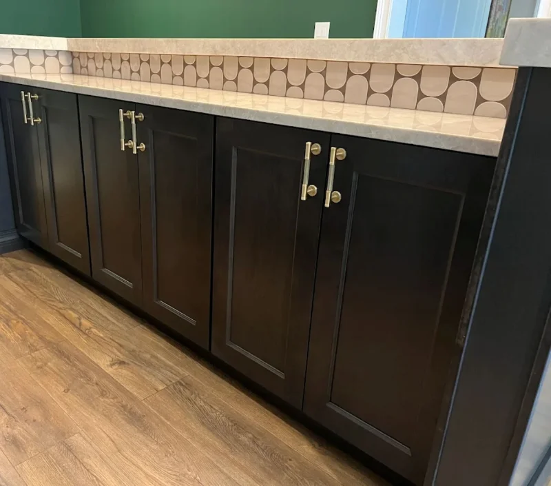 Close-up view of dark charcoal kitchen base cabinets with brushed brass t-bar handles.