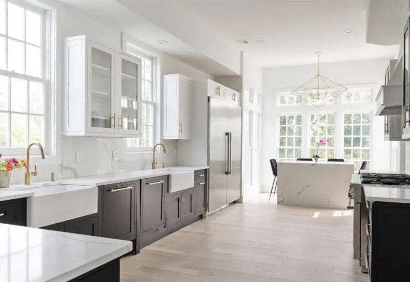 Modern kitchen with dark lower cabinets, white countertops, and bright upper windows.