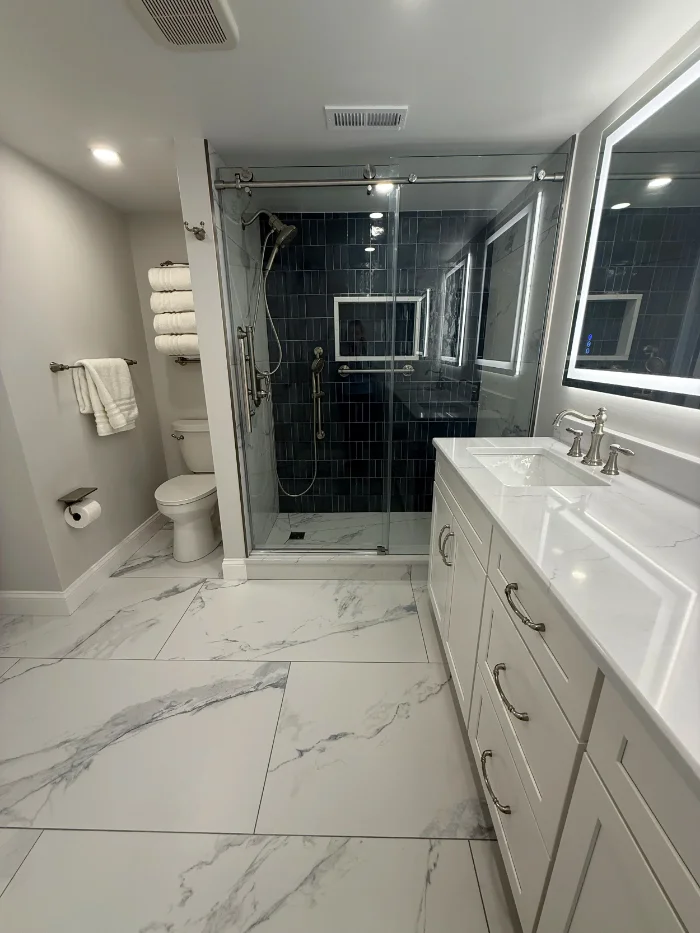 Spacious primary bathroom showing a long white vanity and marble look floor tile.