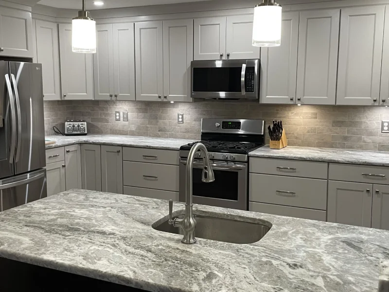 Modern light gray kitchen cabinets featuring stainless steel appliances and granite island.