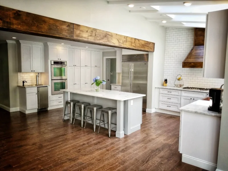 Luxury open concept white kitchen featuring a large island and rustic beam.