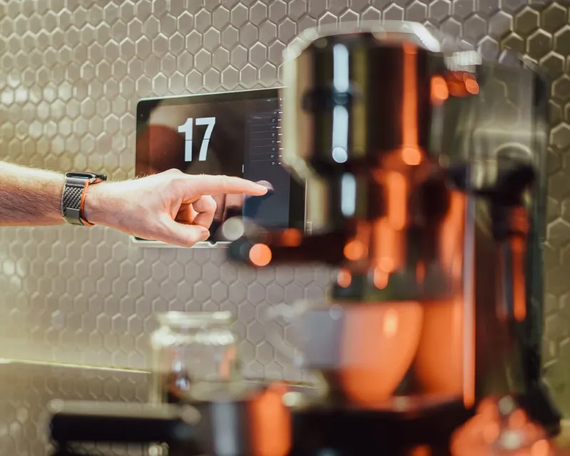 Person using a digital touch screen next to an espresso machine.