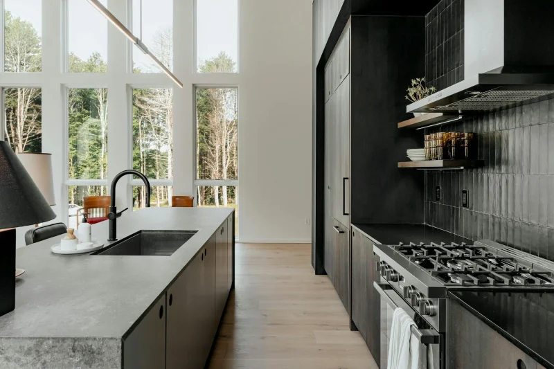 Modern matte black kitchen with concrete island and large windows.