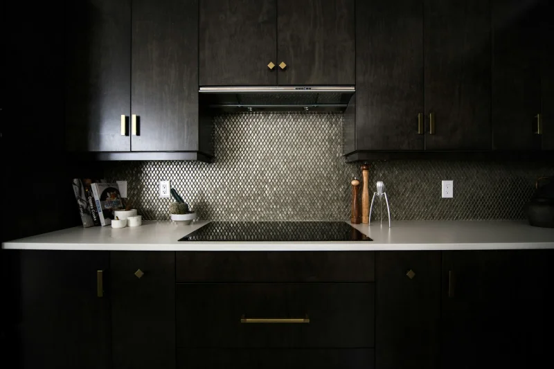 Contemporary kitchen featuring dark charcoal cabinets and illuminated white stone countertops.